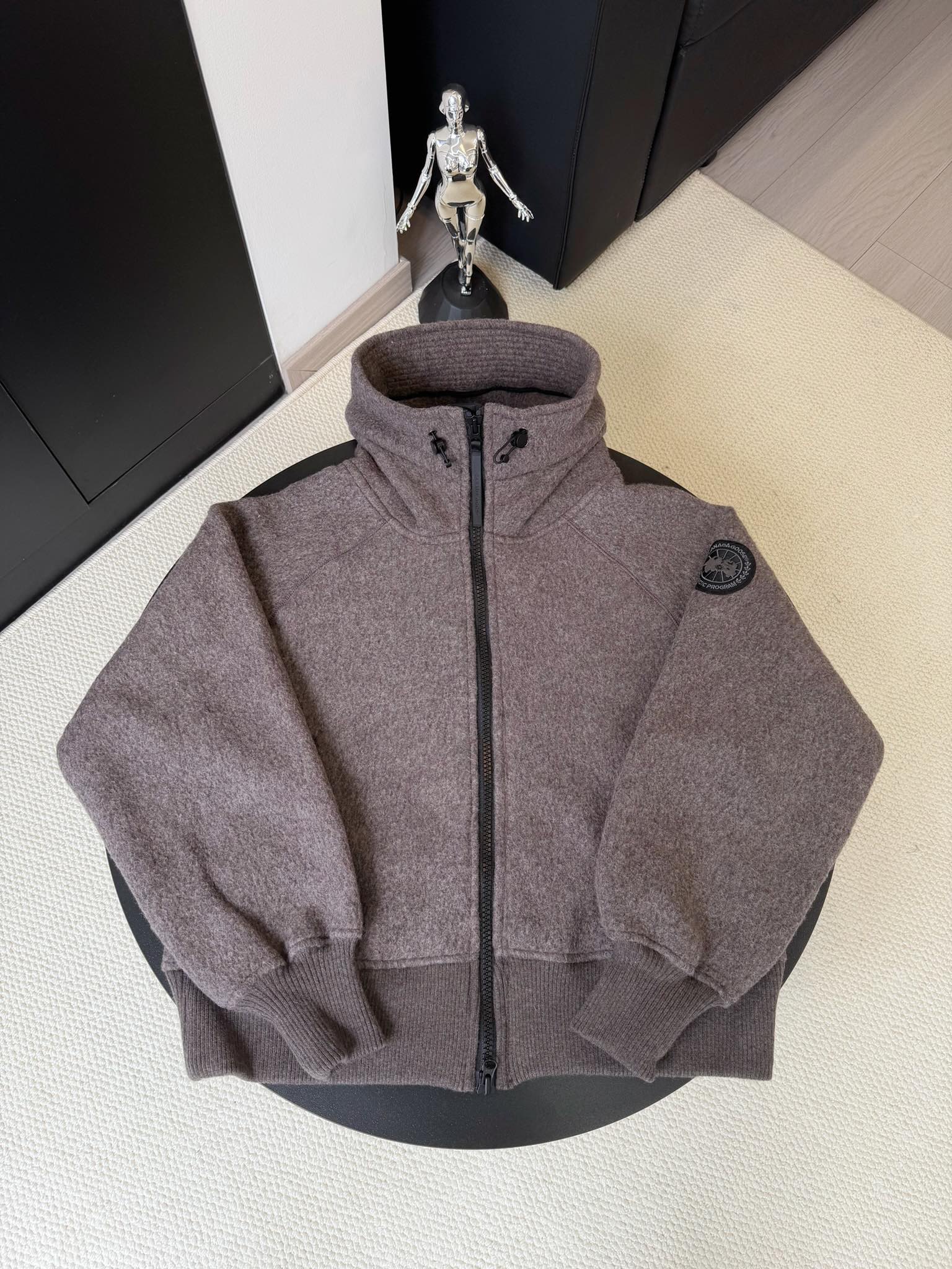 大鹅/Canada Goose抓绒羊毛饰章连帽夹克外套 面料选择: 以羊毛为主体，加入极少量氨纶和聚酯纤维混纺而成的羊毛抓绒面料。羊毛作为核心天然成分，提供无与伦比的温度调节、抑菌防臭和亲肤感。少量氨纶的喂入赋予了面料一定的四向弹性，日常活动时毫无束缚感。作为抓绒结构的基础，聚酯纤维增强了面料的耐久性、抗皱性和快干性，它构成了抓绒的蓬松感，并提供锁住空气等功能。 细节1: 衣袖和下摆采用2乘2罗纹收口，其强大的弹性，可以紧密贴合不同粗细的手腕和腰部，形成一个有效的&lsquo;密封&rsquo;,防止冷风倒灌。在多次拉伸和使用后仍能保持原有形状，不易松垮变形。且罗纹袖口能传递一种设计感，强化视觉美观度。 细节2: 兜帽设计与松紧扣的搭配提升穿戴时的保暖度与防风性能。 辅料:定制弹性抽绳松紧扣定制拉链吊坠定制臂章 尺码：S M L 颜色：黑 灰 咖 米 粉