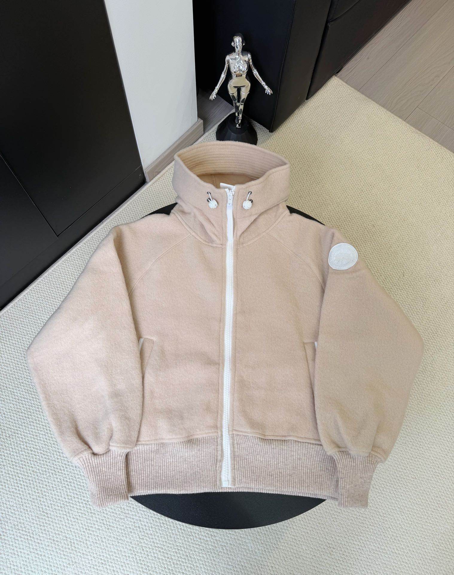 大鹅/Canada Goose抓绒羊毛饰章连帽夹克外套 面料选择: 以羊毛为主体，加入极少量氨纶和聚酯纤维混纺而成的羊毛抓绒面料。羊毛作为核心天然成分，提供无与伦比的温度调节、抑菌防臭和亲肤感。少量氨纶的喂入赋予了面料一定的四向弹性，日常活动时毫无束缚感。作为抓绒结构的基础，聚酯纤维增强了面料的耐久性、抗皱性和快干性，它构成了抓绒的蓬松感，并提供锁住空气等功能。 细节1: 衣袖和下摆采用2乘2罗纹收口，其强大的弹性，可以紧密贴合不同粗细的手腕和腰部，形成一个有效的&lsquo;密封&rsquo;,防止冷风倒灌。在多次拉伸和使用后仍能保持原有形状，不易松垮变形。且罗纹袖口能传递一种设计感，强化视觉美观度。 细节2: 兜帽设计与松紧扣的搭配提升穿戴时的保暖度与防风性能。 辅料:定制弹性抽绳松紧扣定制拉链吊坠定制臂章 尺码：S M L 颜色：黑 灰 咖 米 粉