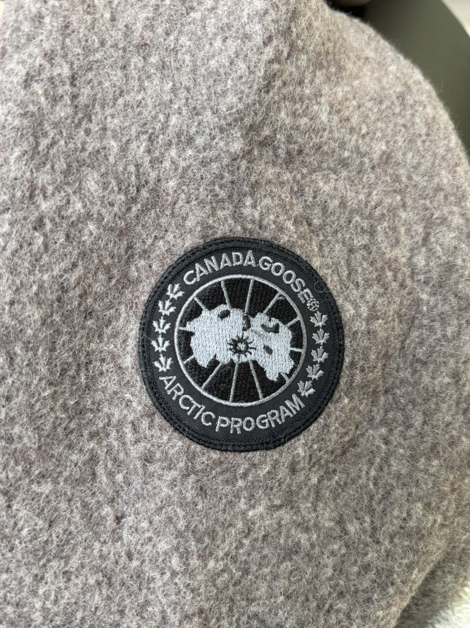 大鹅/Canada Goose抓绒羊毛饰章连帽夹克外套 面料选择: 以羊毛为主体，加入极少量氨纶和聚酯纤维混纺而成的羊毛抓绒面料。羊毛作为核心天然成分，提供无与伦比的温度调节、抑菌防臭和亲肤感。少量氨纶的喂入赋予了面料一定的四向弹性，日常活动时毫无束缚感。作为抓绒结构的基础，聚酯纤维增强了面料的耐久性、抗皱性和快干性，它构成了抓绒的蓬松感，并提供锁住空气等功能。 细节1: 衣袖和下摆采用2乘2罗纹收口，其强大的弹性，可以紧密贴合不同粗细的手腕和腰部，形成一个有效的&lsquo;密封&rsquo;,防止冷风倒灌。在多次拉伸和使用后仍能保持原有形状，不易松垮变形。且罗纹袖口能传递一种设计感，强化视觉美观度。 细节2: 兜帽设计与松紧扣的搭配提升穿戴时的保暖度与防风性能。 辅料:定制弹性抽绳松紧扣定制拉链吊坠定制臂章 尺码：S M L 颜色：黑 灰 咖 米 粉