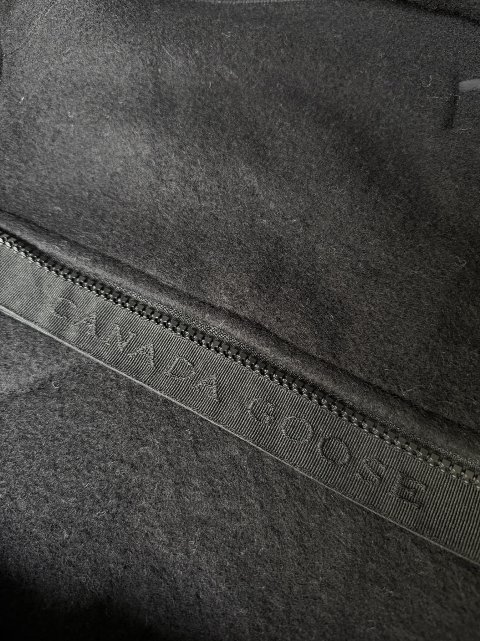 大鹅/Canada Goose抓绒羊毛饰章连帽夹克外套 面料选择: 以羊毛为主体，加入极少量氨纶和聚酯纤维混纺而成的羊毛抓绒面料。羊毛作为核心天然成分，提供无与伦比的温度调节、抑菌防臭和亲肤感。少量氨纶的喂入赋予了面料一定的四向弹性，日常活动时毫无束缚感。作为抓绒结构的基础，聚酯纤维增强了面料的耐久性、抗皱性和快干性，它构成了抓绒的蓬松感，并提供锁住空气等功能。 细节1: 衣袖和下摆采用2乘2罗纹收口，其强大的弹性，可以紧密贴合不同粗细的手腕和腰部，形成一个有效的&lsquo;密封&rsquo;,防止冷风倒灌。在多次拉伸和使用后仍能保持原有形状，不易松垮变形。且罗纹袖口能传递一种设计感，强化视觉美观度。 细节2: 兜帽设计与松紧扣的搭配提升穿戴时的保暖度与防风性能。 辅料:定制弹性抽绳松紧扣定制拉链吊坠定制臂章 尺码：S M L 颜色：黑 灰 咖 米 粉