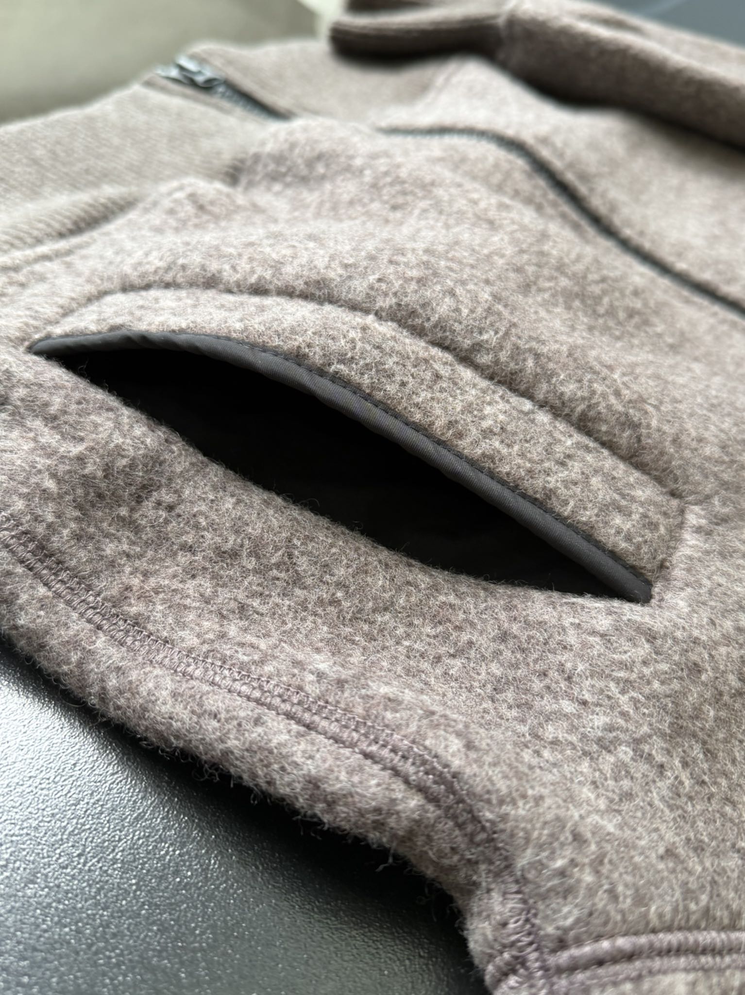 大鹅/Canada Goose抓绒羊毛饰章连帽夹克外套 面料选择: 以羊毛为主体，加入极少量氨纶和聚酯纤维混纺而成的羊毛抓绒面料。羊毛作为核心天然成分，提供无与伦比的温度调节、抑菌防臭和亲肤感。少量氨纶的喂入赋予了面料一定的四向弹性，日常活动时毫无束缚感。作为抓绒结构的基础，聚酯纤维增强了面料的耐久性、抗皱性和快干性，它构成了抓绒的蓬松感，并提供锁住空气等功能。 细节1: 衣袖和下摆采用2乘2罗纹收口，其强大的弹性，可以紧密贴合不同粗细的手腕和腰部，形成一个有效的&lsquo;密封&rsquo;,防止冷风倒灌。在多次拉伸和使用后仍能保持原有形状，不易松垮变形。且罗纹袖口能传递一种设计感，强化视觉美观度。 细节2: 兜帽设计与松紧扣的搭配提升穿戴时的保暖度与防风性能。 辅料:定制弹性抽绳松紧扣定制拉链吊坠定制臂章 尺码：S M L 颜色：黑 灰 咖 米 粉