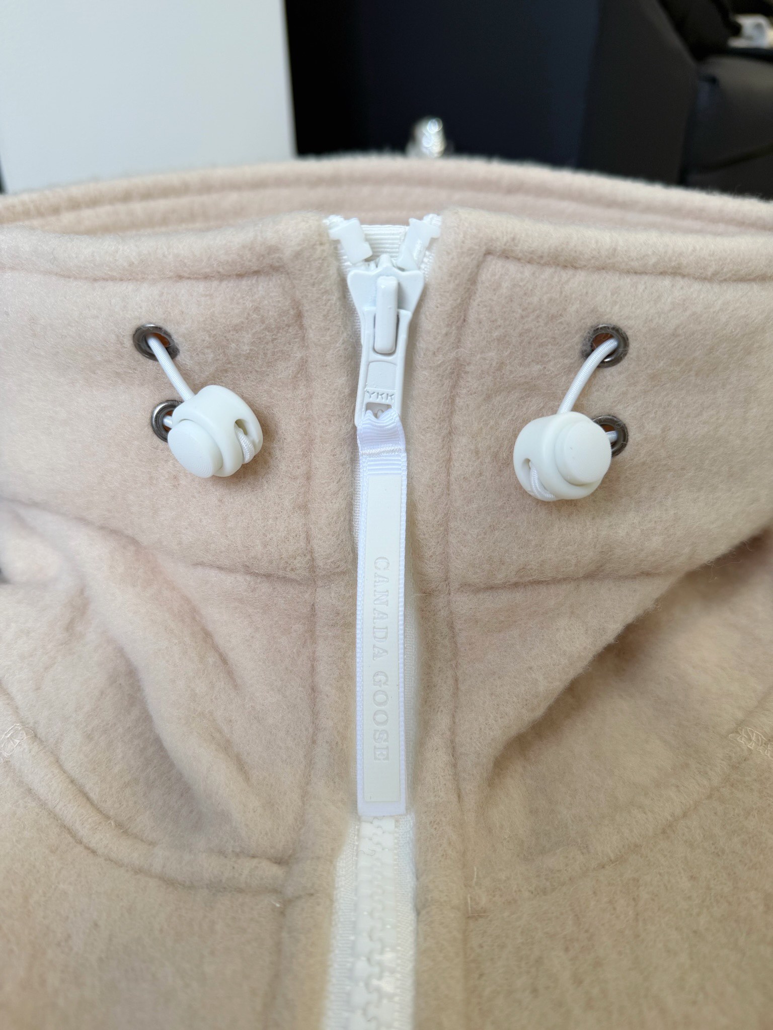 大鹅/Canada Goose抓绒羊毛饰章连帽夹克外套 面料选择: 以羊毛为主体，加入极少量氨纶和聚酯纤维混纺而成的羊毛抓绒面料。羊毛作为核心天然成分，提供无与伦比的温度调节、抑菌防臭和亲肤感。少量氨纶的喂入赋予了面料一定的四向弹性，日常活动时毫无束缚感。作为抓绒结构的基础，聚酯纤维增强了面料的耐久性、抗皱性和快干性，它构成了抓绒的蓬松感，并提供锁住空气等功能。 细节1: 衣袖和下摆采用2乘2罗纹收口，其强大的弹性，可以紧密贴合不同粗细的手腕和腰部，形成一个有效的&lsquo;密封&rsquo;,防止冷风倒灌。在多次拉伸和使用后仍能保持原有形状，不易松垮变形。且罗纹袖口能传递一种设计感，强化视觉美观度。 细节2: 兜帽设计与松紧扣的搭配提升穿戴时的保暖度与防风性能。 辅料:定制弹性抽绳松紧扣定制拉链吊坠定制臂章 尺码：S M L 颜色：黑 灰 咖 米 粉