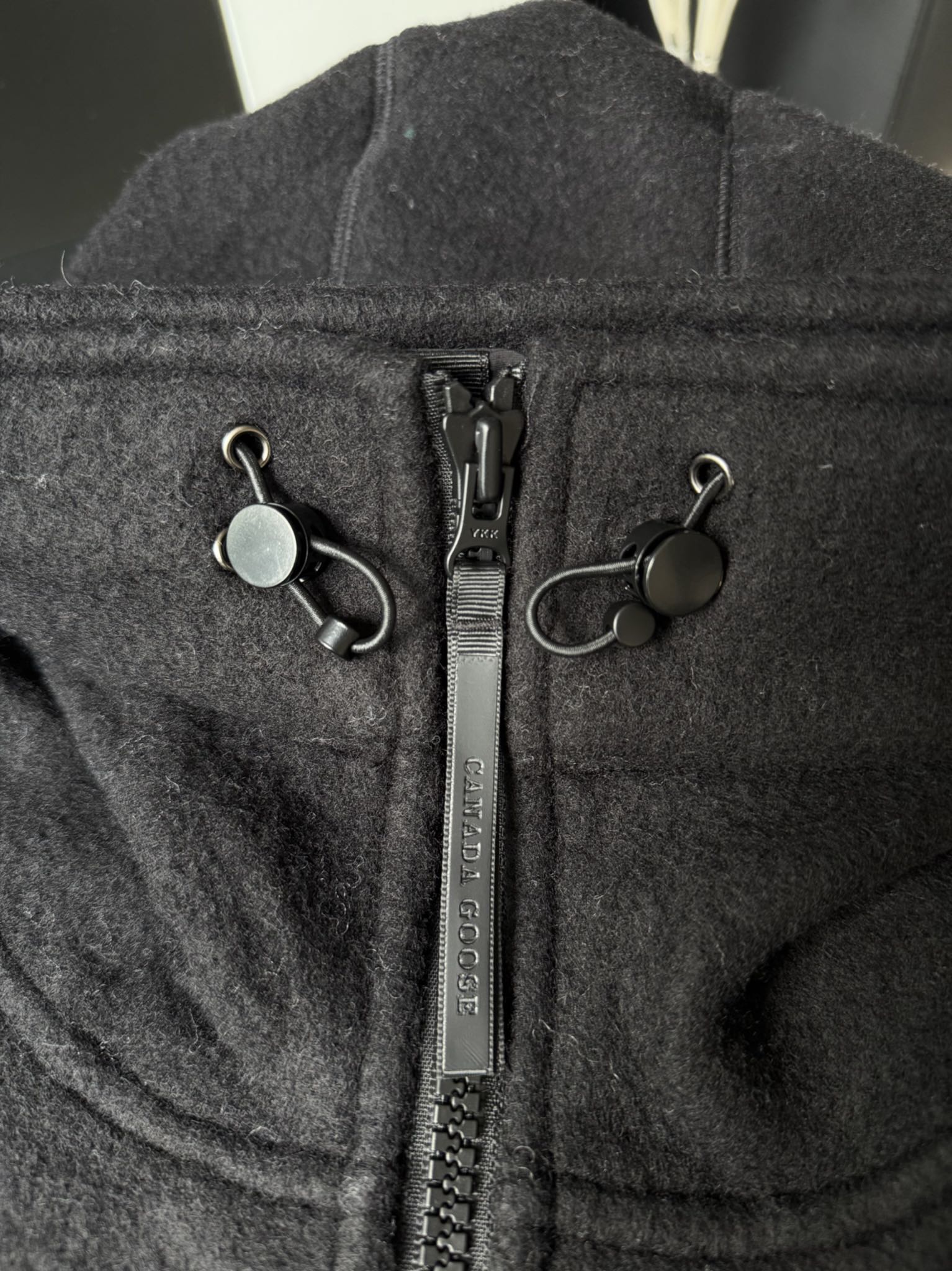 大鹅/Canada Goose抓绒羊毛饰章连帽夹克外套 面料选择: 以羊毛为主体，加入极少量氨纶和聚酯纤维混纺而成的羊毛抓绒面料。羊毛作为核心天然成分，提供无与伦比的温度调节、抑菌防臭和亲肤感。少量氨纶的喂入赋予了面料一定的四向弹性，日常活动时毫无束缚感。作为抓绒结构的基础，聚酯纤维增强了面料的耐久性、抗皱性和快干性，它构成了抓绒的蓬松感，并提供锁住空气等功能。 细节1: 衣袖和下摆采用2乘2罗纹收口，其强大的弹性，可以紧密贴合不同粗细的手腕和腰部，形成一个有效的&lsquo;密封&rsquo;,防止冷风倒灌。在多次拉伸和使用后仍能保持原有形状，不易松垮变形。且罗纹袖口能传递一种设计感，强化视觉美观度。 细节2: 兜帽设计与松紧扣的搭配提升穿戴时的保暖度与防风性能。 辅料:定制弹性抽绳松紧扣定制拉链吊坠定制臂章 尺码：S M L 颜色：黑 灰 咖 米 粉