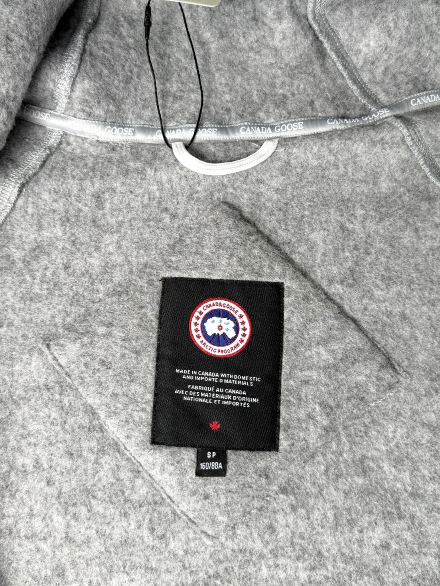 大鹅/Canada Goose抓绒羊毛饰章连帽夹克外套 面料选择: 以羊毛为主体，加入极少量氨纶和聚酯纤维混纺而成的羊毛抓绒面料。羊毛作为核心天然成分，提供无与伦比的温度调节、抑菌防臭和亲肤感。少量氨纶的喂入赋予了面料一定的四向弹性，日常活动时毫无束缚感。作为抓绒结构的基础，聚酯纤维增强了面料的耐久性、抗皱性和快干性，它构成了抓绒的蓬松感，并提供锁住空气等功能。 细节1: 衣袖和下摆采用2乘2罗纹收口，其强大的弹性，可以紧密贴合不同粗细的手腕和腰部，形成一个有效的&lsquo;密封&rsquo;,防止冷风倒灌。在多次拉伸和使用后仍能保持原有形状，不易松垮变形。且罗纹袖口能传递一种设计感，强化视觉美观度。 细节2: 兜帽设计与松紧扣的搭配提升穿戴时的保暖度与防风性能。 辅料:定制弹性抽绳松紧扣定制拉链吊坠定制臂章 尺码：S M L 颜色：黑 灰 咖 米 粉