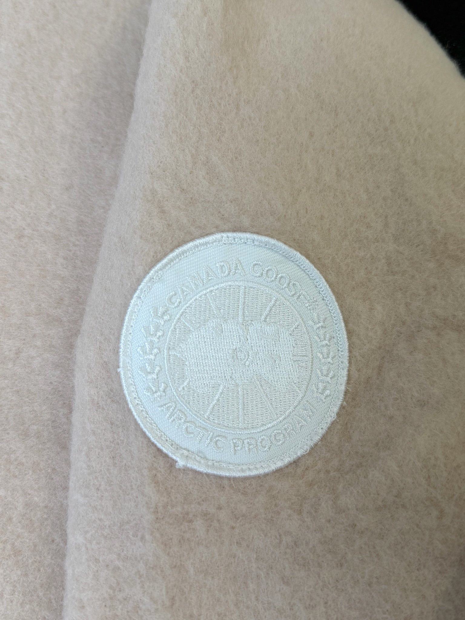 大鹅/Canada Goose抓绒羊毛饰章连帽夹克外套 面料选择: 以羊毛为主体，加入极少量氨纶和聚酯纤维混纺而成的羊毛抓绒面料。羊毛作为核心天然成分，提供无与伦比的温度调节、抑菌防臭和亲肤感。少量氨纶的喂入赋予了面料一定的四向弹性，日常活动时毫无束缚感。作为抓绒结构的基础，聚酯纤维增强了面料的耐久性、抗皱性和快干性，它构成了抓绒的蓬松感，并提供锁住空气等功能。 细节1: 衣袖和下摆采用2乘2罗纹收口，其强大的弹性，可以紧密贴合不同粗细的手腕和腰部，形成一个有效的&lsquo;密封&rsquo;,防止冷风倒灌。在多次拉伸和使用后仍能保持原有形状，不易松垮变形。且罗纹袖口能传递一种设计感，强化视觉美观度。 细节2: 兜帽设计与松紧扣的搭配提升穿戴时的保暖度与防风性能。 辅料:定制弹性抽绳松紧扣定制拉链吊坠定制臂章 尺码：S M L 颜色：黑 灰 咖 米 粉