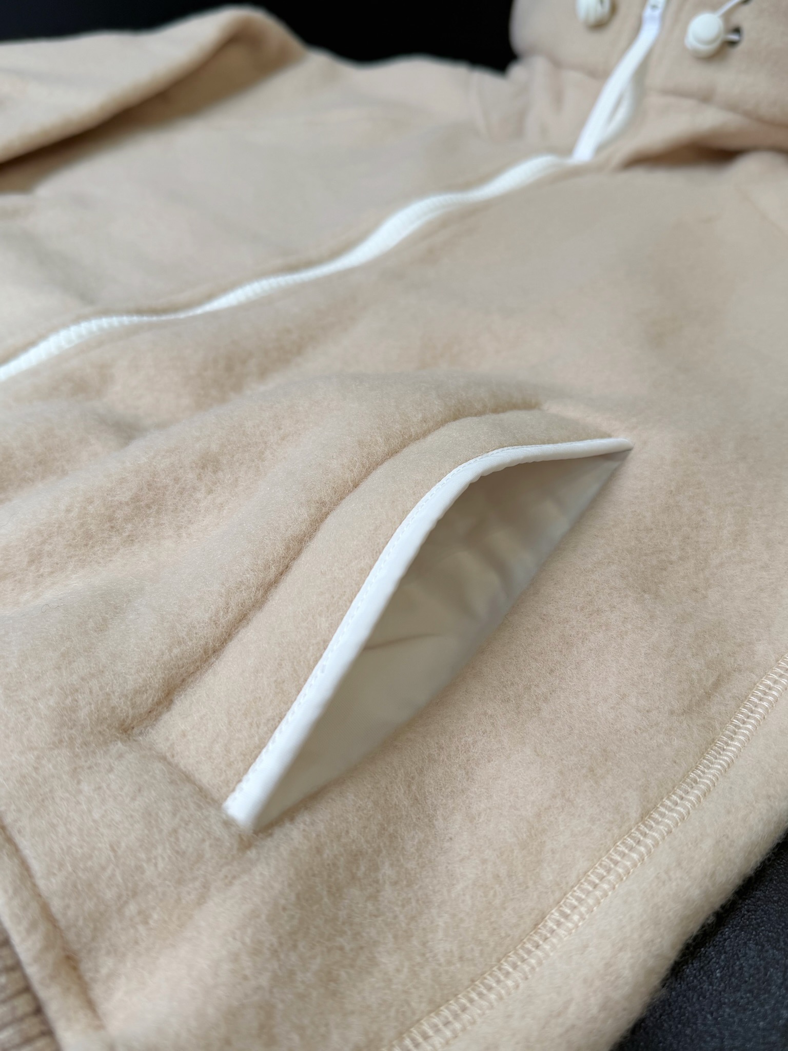 大鹅/Canada Goose抓绒羊毛饰章连帽夹克外套 面料选择: 以羊毛为主体，加入极少量氨纶和聚酯纤维混纺而成的羊毛抓绒面料。羊毛作为核心天然成分，提供无与伦比的温度调节、抑菌防臭和亲肤感。少量氨纶的喂入赋予了面料一定的四向弹性，日常活动时毫无束缚感。作为抓绒结构的基础，聚酯纤维增强了面料的耐久性、抗皱性和快干性，它构成了抓绒的蓬松感，并提供锁住空气等功能。 细节1: 衣袖和下摆采用2乘2罗纹收口，其强大的弹性，可以紧密贴合不同粗细的手腕和腰部，形成一个有效的&lsquo;密封&rsquo;,防止冷风倒灌。在多次拉伸和使用后仍能保持原有形状，不易松垮变形。且罗纹袖口能传递一种设计感，强化视觉美观度。 细节2: 兜帽设计与松紧扣的搭配提升穿戴时的保暖度与防风性能。 辅料:定制弹性抽绳松紧扣定制拉链吊坠定制臂章 尺码：S M L 颜色：黑 灰 咖 米 粉