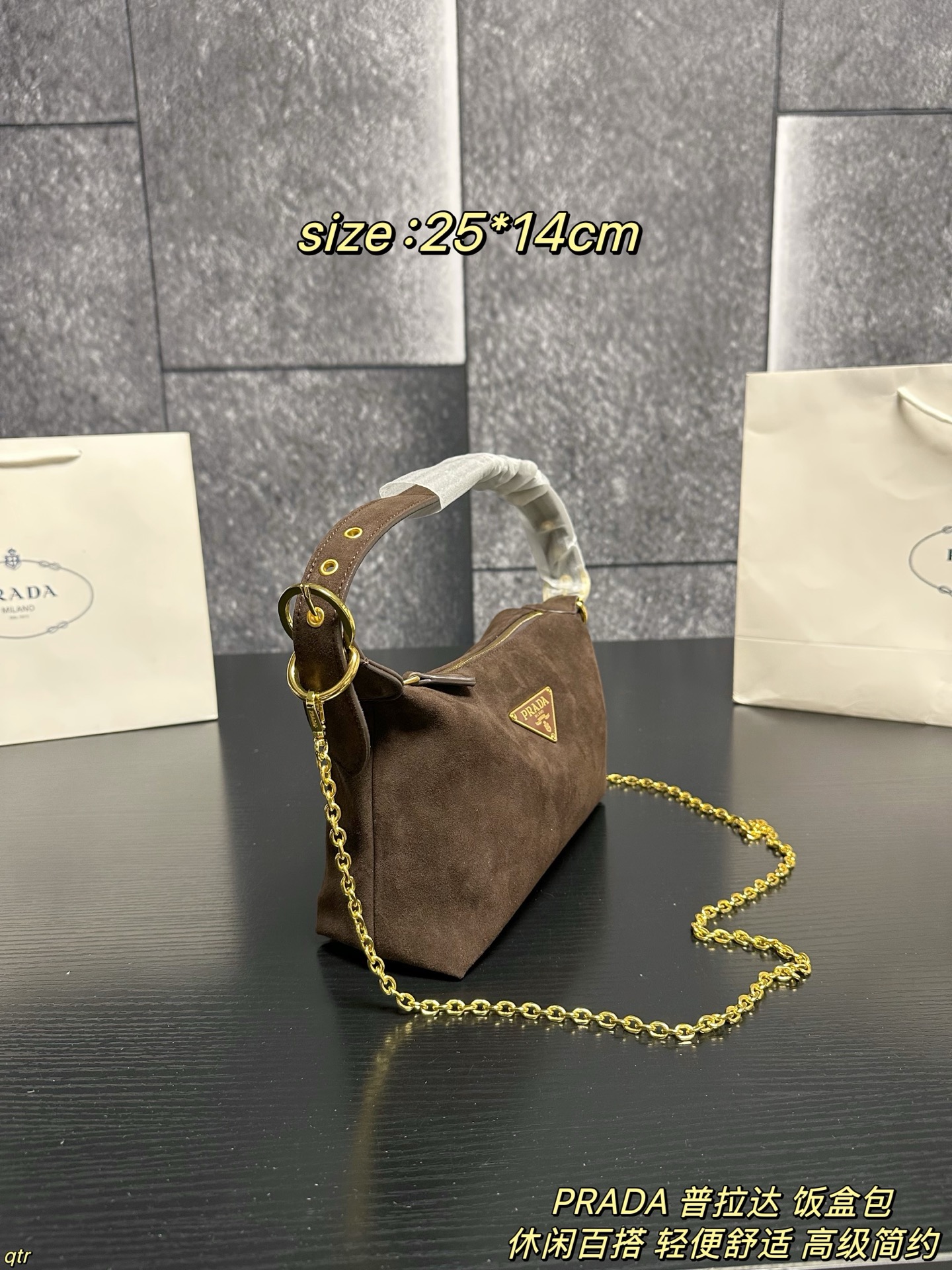 P105配盒 PRADA 普拉达 饭盒包 这款包采用进口麂皮，具有柔软的轮廓和多个口袋，轻质实用的Re-Nylon强调了设计的多功能风格，而皮革细节和标志性点缀则反映了Prada的手工传统，配有2条可拆卸、可调节的编织标志带肩带，容量空间大，上身效果非常时尚。又是一款永久不过时爆款。值得拥有 尺寸：25*14cm